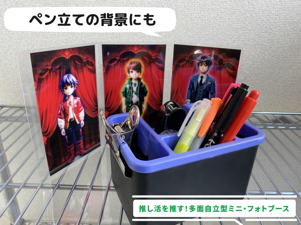 金属製の棚の上に置かれたペン立て。ペン立ての背景には、アニメ風の男性キャラクターのイラストが描かれた三連のミニフォトブースプレートが立てかけられている。