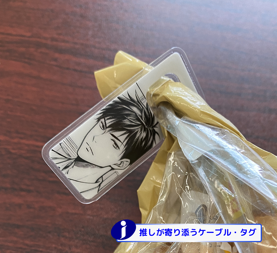 白いケーブルと金色の袋に留められた透明なケーブルタグ。タグには男性漫画キャラクターのイラストが印刷